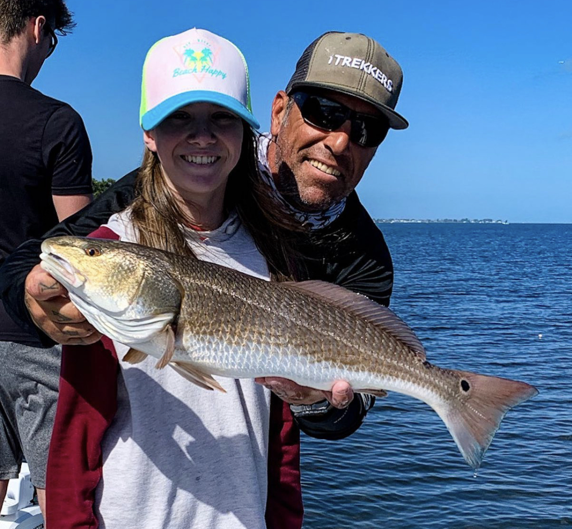 a picture of a fisherman holding a redfish caught in Sarasota, along Tampa Bay, with others on boat in the background.